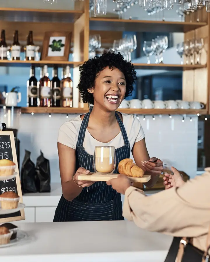 A smiling barista serving coffee and a croissant across the café counter