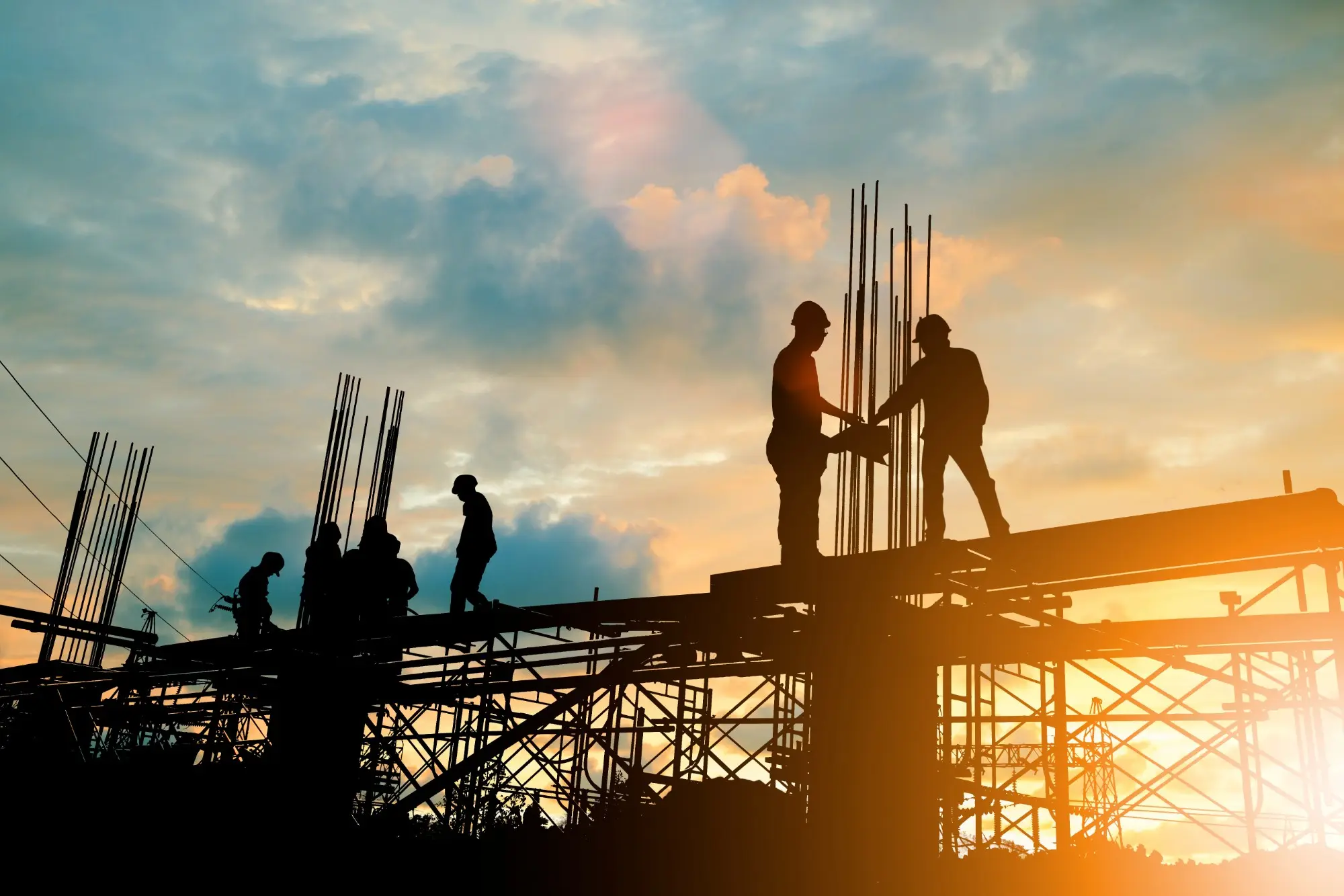 A construction crew at work on a building's framework at sunset